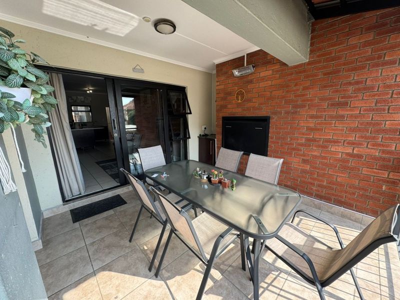 A covered patio area featuring tiled flooring, an exposed brick wall, and a built-in braai, providing a functional outdoor entertainment space.