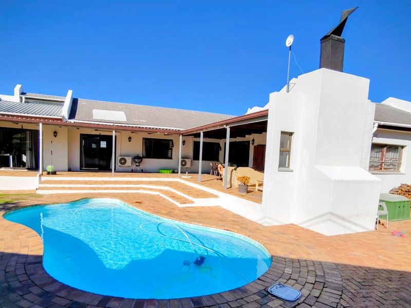 Rear exterior view featuring a swimming pool, brick paved patio area, and a covered outdoor space with a built-in fireplace.