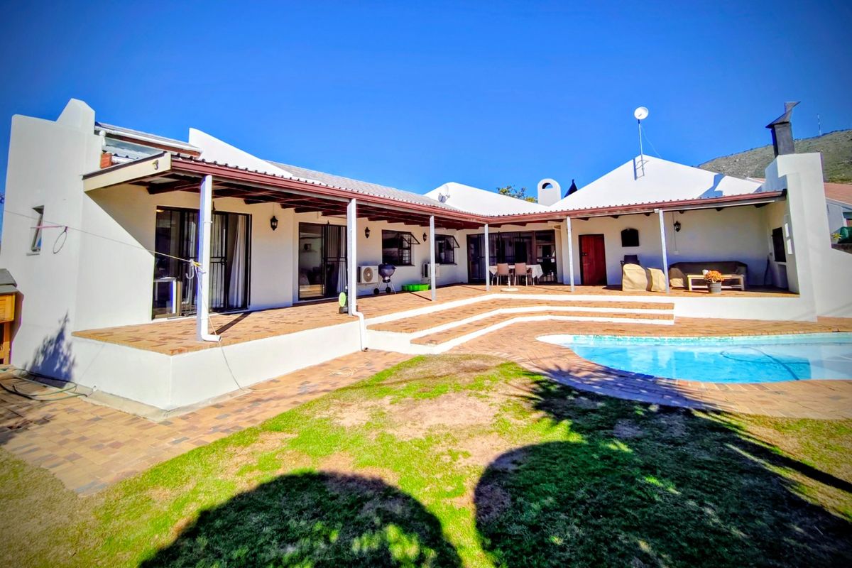 Spacious rear exterior featuring a covered patio, brick-paved entertainment area, and a swimming pool set against a white-walled house structure.