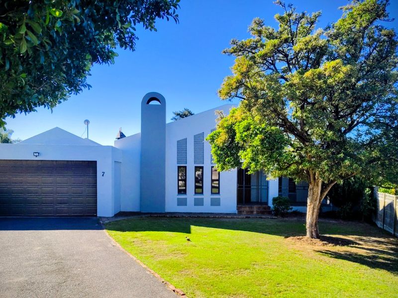 Front elevation of a modern house featuring a double garage, paved driveway, and a well-maintained front garden with mature trees.