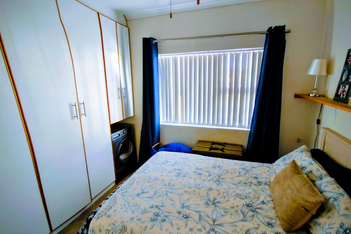 A bedroom featuring built-in cupboards with an integrated laundry appliance space, a ceiling fan, and vertical window blinds.