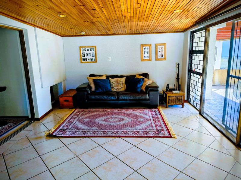 A living room featuring a warm timber tongue and groove ceiling, ceramic tiled flooring, and large sliding glass doors providing access to the patio.