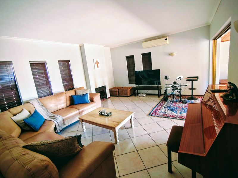 Spacious living room featuring tiled flooring, a built-in fireplace, and a wall-mounted air conditioning unit, offering a comfortable and functional family space.