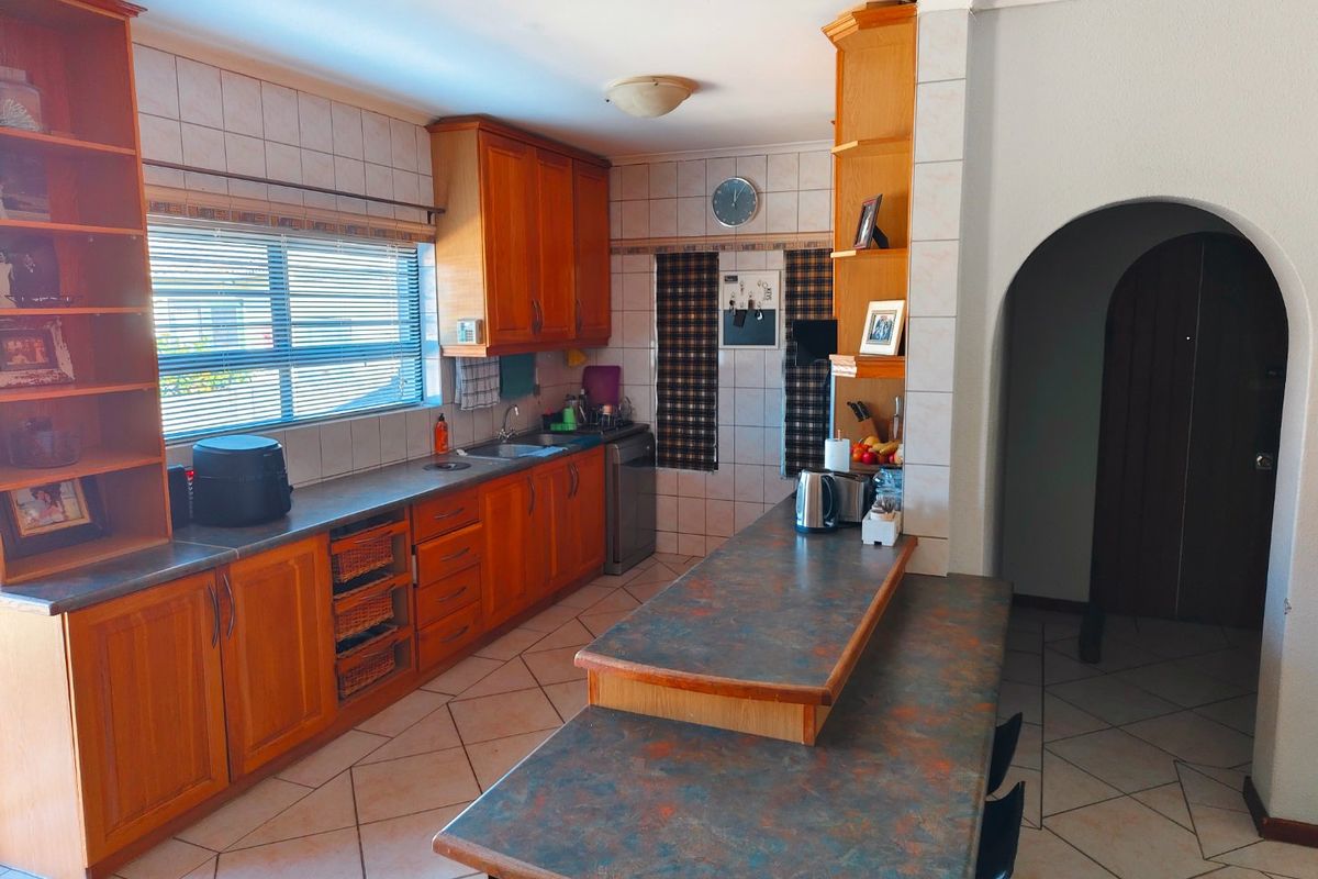 A functional kitchen featuring wooden cabinetry, laminate countertops, a breakfast bar, and tiled flooring, with an arched entryway leading to adjacent living spaces.