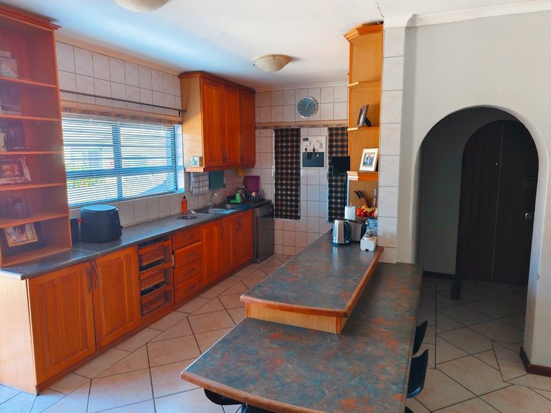 A functional kitchen featuring wooden cabinetry, laminate countertops, a breakfast bar, and tiled flooring, with an arched entryway leading to adjacent living spaces.