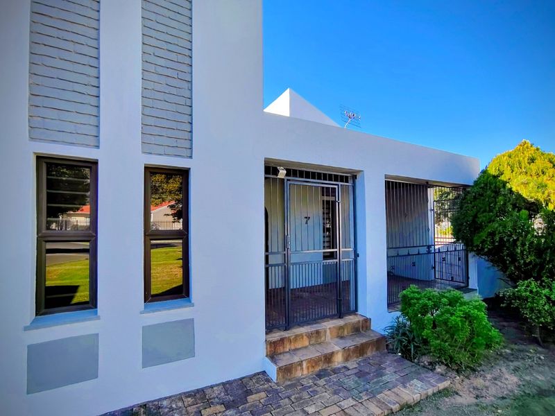 Front facade of the house featuring a secure entrance with security gate, brick detailing, and paved walkway access.