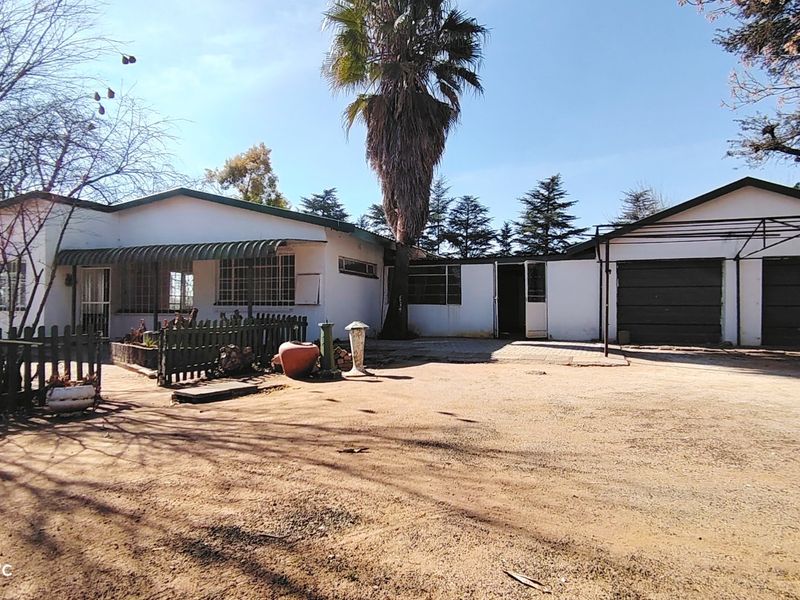 Front exterior view of a farm property featuring a main dwelling with a covered patio, security bars, and an attached double garage.