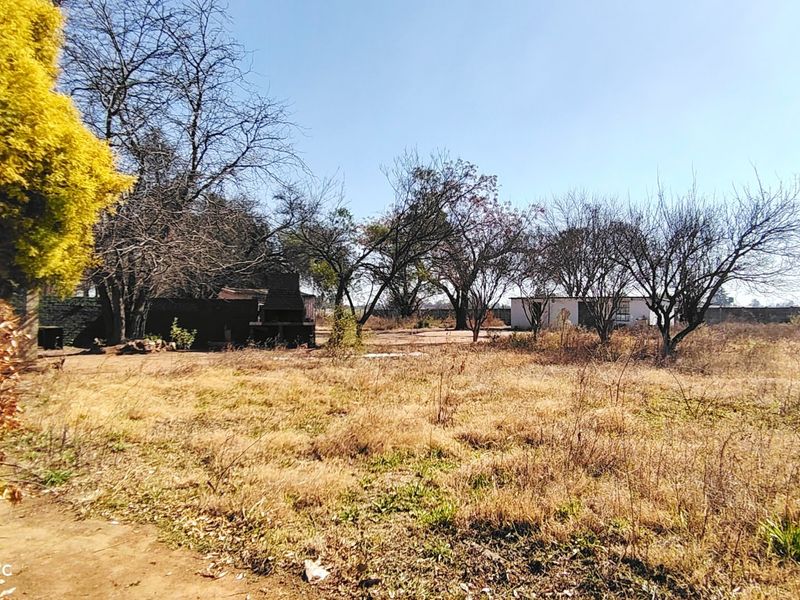 Expansive farm garden area featuring a built-in outdoor braai and perimeter walling, set against a backdrop of mature trees.