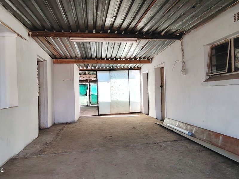 An unfinished utility or storage space featuring a corrugated metal ceiling, concrete flooring, and direct access to an outdoor area via a sliding door.