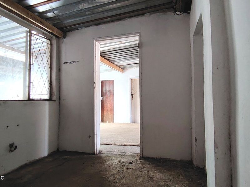 An empty, unfinished utility space featuring exposed corrugated metal ceilings, concrete flooring, and basic timber door frames, requiring significant renovation.