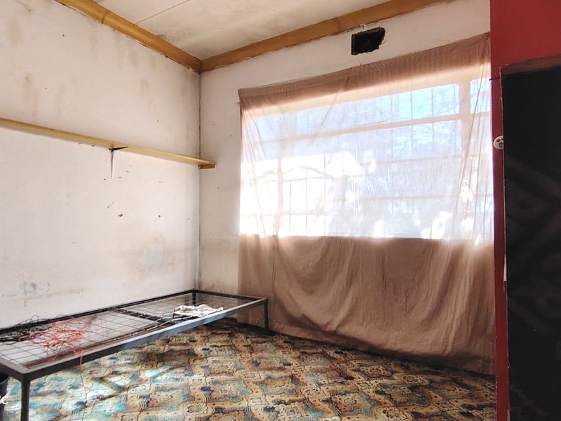 A bedroom space requiring significant renovation, featuring worn carpet flooring and damaged wall finishes.