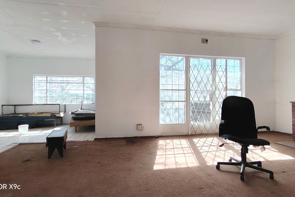 Spacious living area featuring a brick fireplace, security gates, and dual flooring finishes, offering a blank canvas for renovation and modernization.