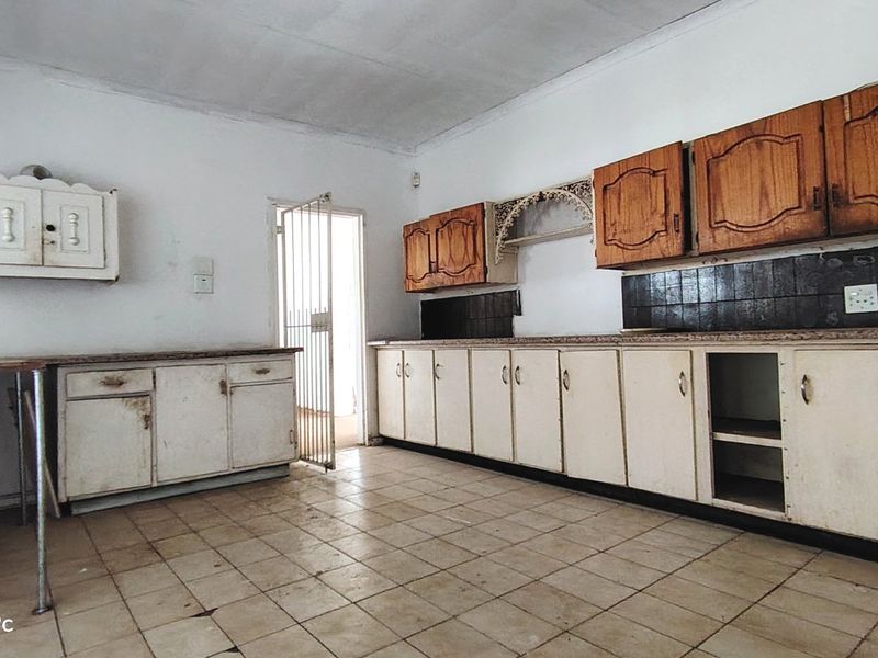 A dated kitchen featuring extensive built-in cabinetry, tiled flooring, and a tiled backsplash, requiring significant cosmetic updates to modernize the space.