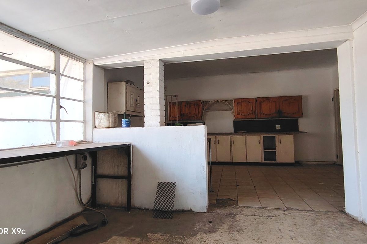 An empty, dated kitchen area featuring original built-in cabinetry, tiled flooring, and a large window, requiring significant renovation and modernization.