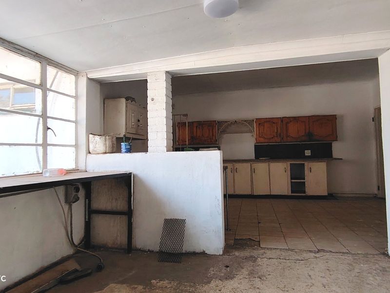 An empty, dated kitchen area featuring original built-in cabinetry, tiled flooring, and a large window, requiring significant renovation and modernization.
