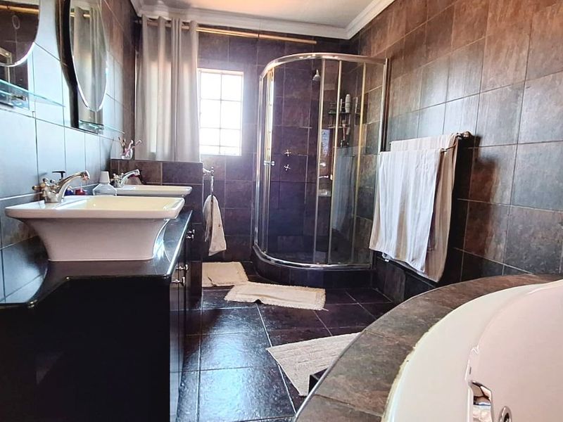 A spacious bathroom featuring a double vanity with vessel sinks, a corner shower enclosure, and a built-in bathtub with dark tiled finishes.