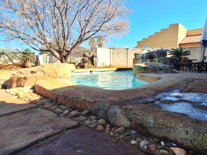 Outdoor pool area featuring a rock-scaped swimming pool, paved patio surround, and perimeter boundary wall.