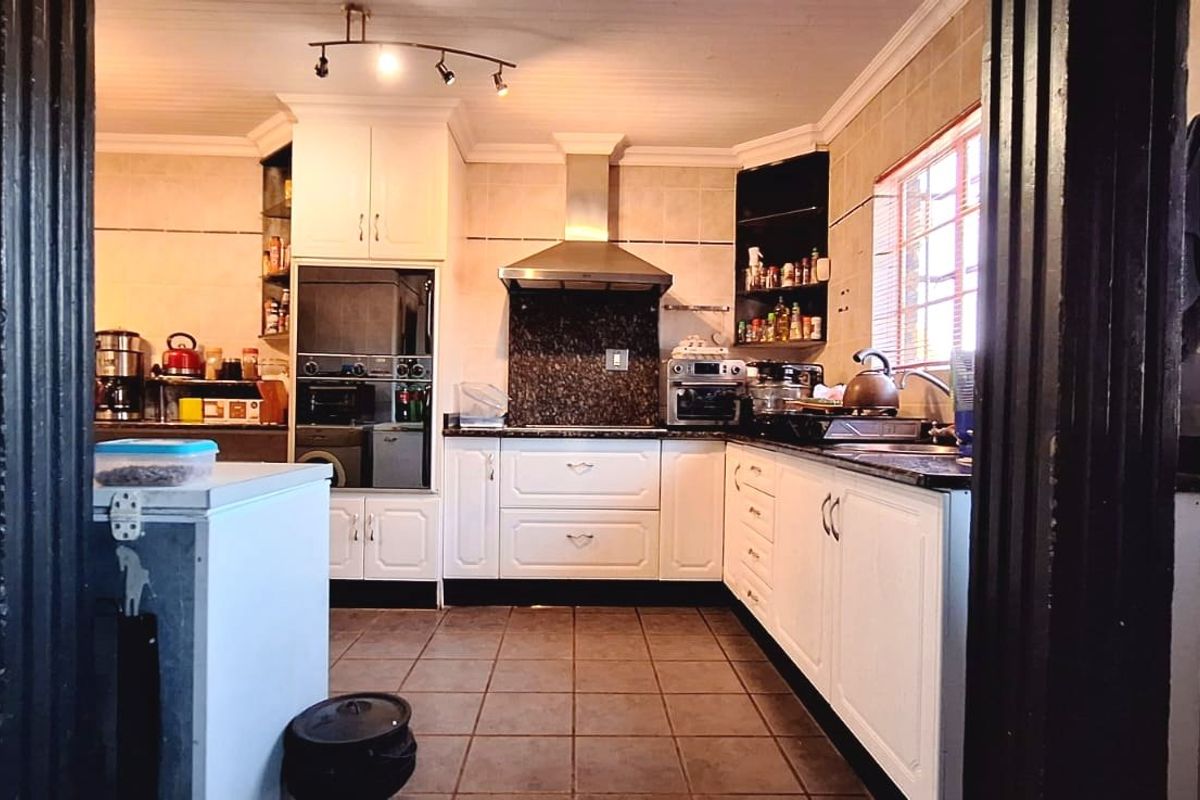A functional kitchen featuring white cabinetry, granite countertops, a built-in oven, and a stainless steel extractor fan with tiled flooring and backsplash.