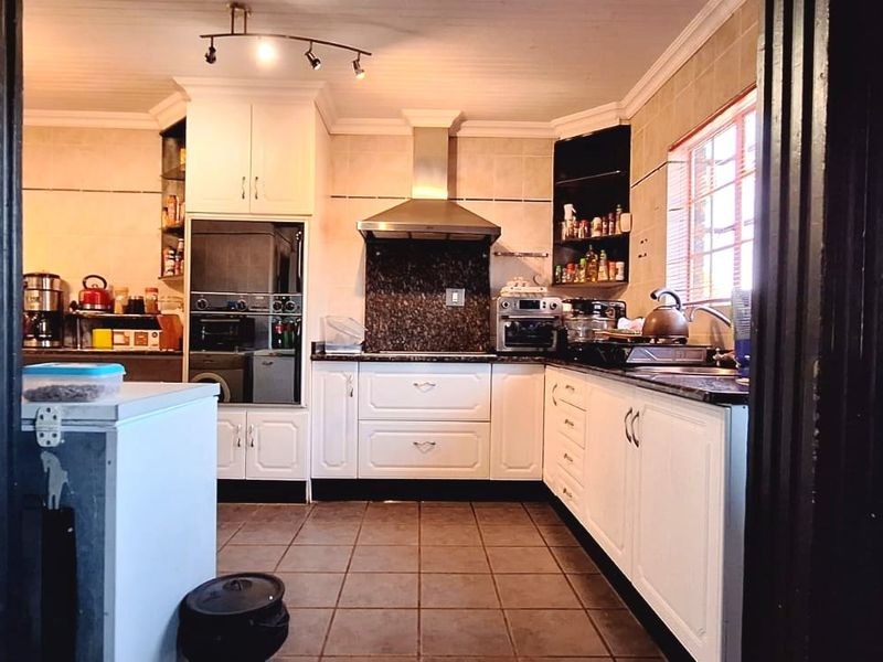 A functional kitchen featuring white cabinetry, granite countertops, a built-in oven, and a stainless steel extractor fan with tiled flooring and backsplash.
