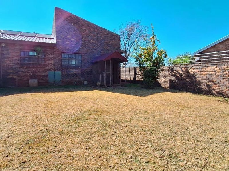 A spacious rear garden featuring face-brick exterior walls, a pitched metal roof, and a secure perimeter brick wall.