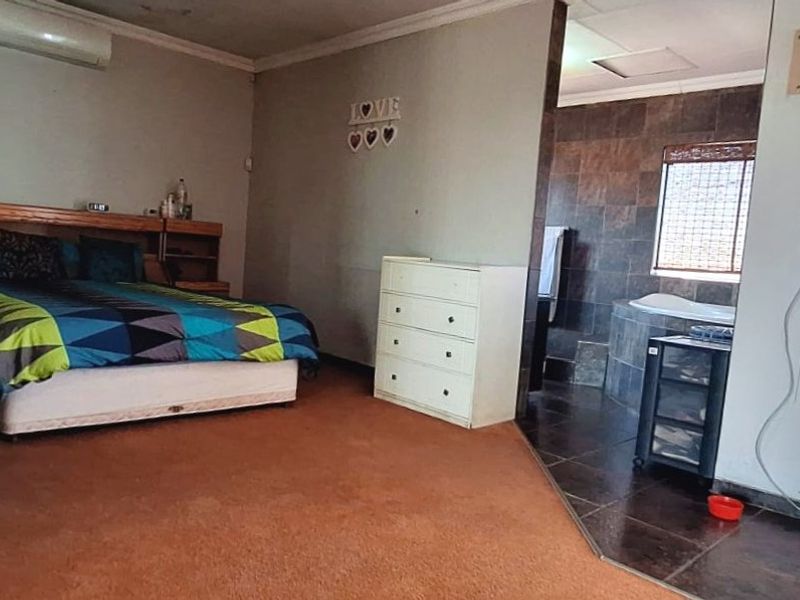 Spacious bedroom featuring an open-plan en-suite bathroom with a built-in bathtub, split-system air conditioning, and direct access to an outdoor area via a security gate.