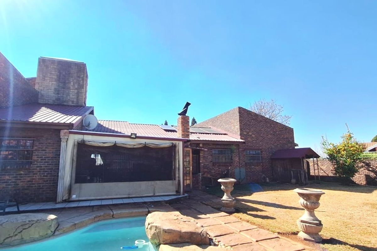 Rear view of a face brick house featuring a swimming pool, paved patio area, and solar water heating panels on the metal roof.