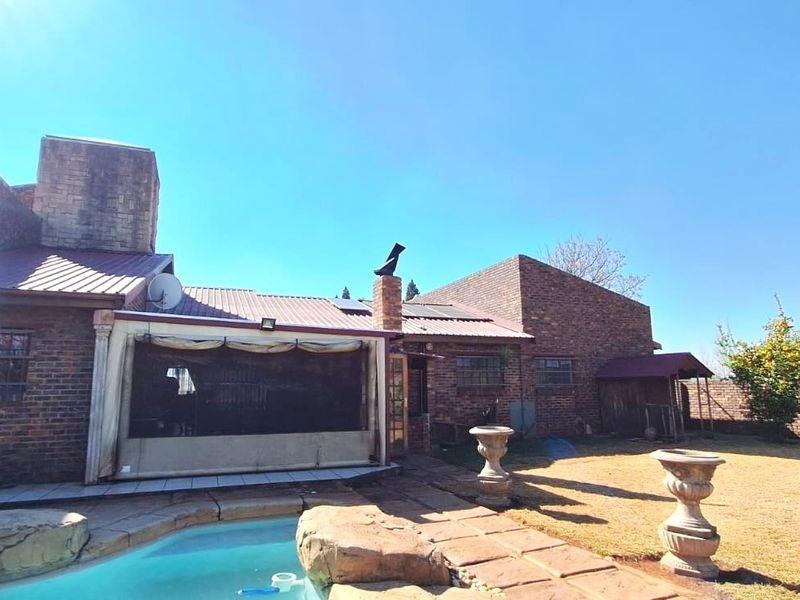 Rear view of a face brick house featuring a swimming pool, paved patio area, and solar water heating panels on the metal roof.