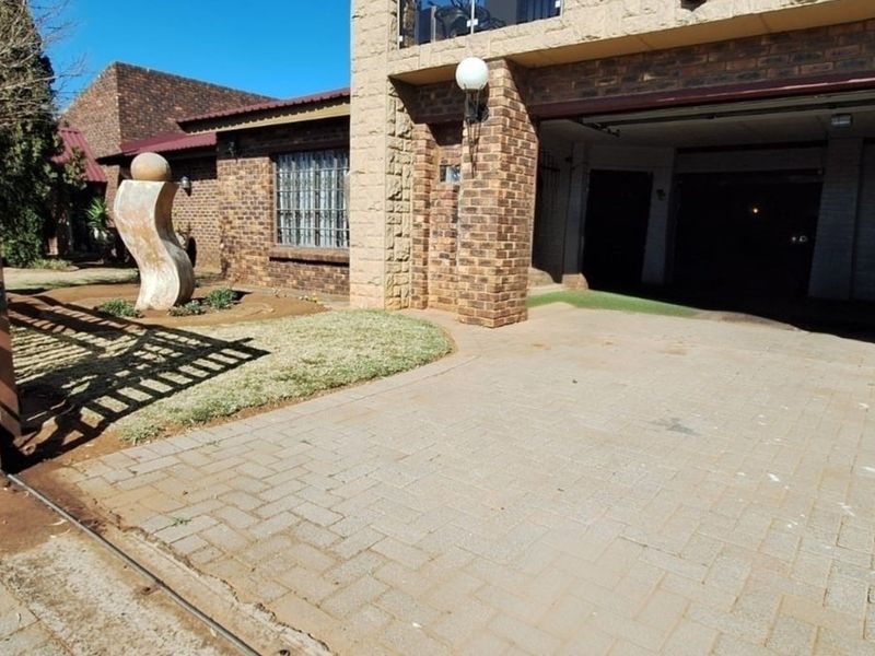 Front exterior view of the property featuring a brick facade, paved driveway, and secure gated entrance.