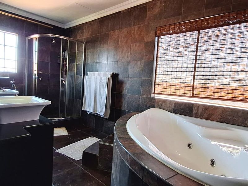 Spacious bathroom featuring a corner spa bath, glass shower enclosure, and a double vanity with dark tiled finishes throughout.