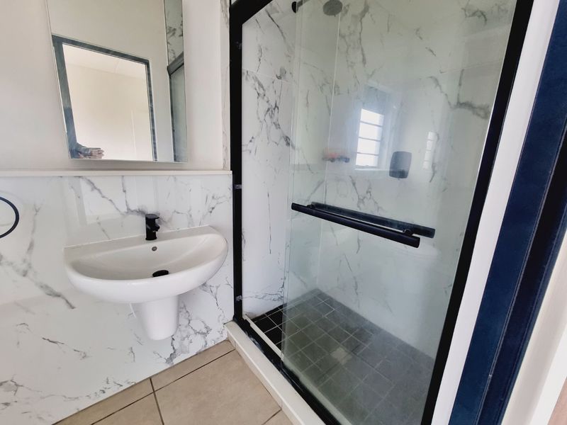 Modern bathroom featuring a pedestal basin with black fixtures, a glass-enclosed shower with marble-look wall tiles, and contemporary finishes.
