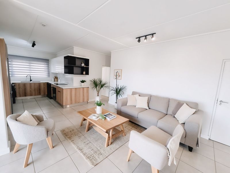 Modern open-plan living area featuring a contemporary kitchen with wood-finish cabinetry, integrated appliances, and neutral tiled flooring throughout.