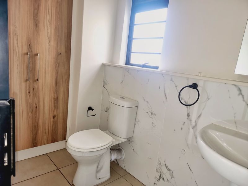 A clean, modern bathroom featuring marble-look wall tiles, a white toilet, a washbasin, and a built-in wooden cupboard for storage.