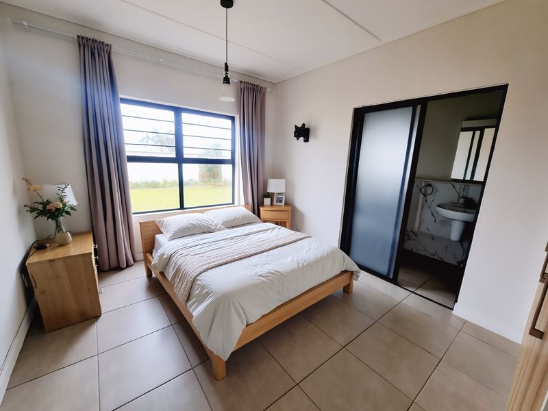 A well-lit bedroom featuring tiled flooring, large windows with curtains, and direct access to an en-suite bathroom with a modern sliding door.