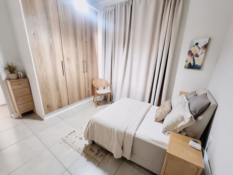 A well-maintained bedroom featuring modern built-in wooden cupboards and neutral tiled flooring, offering a clean and functional living space.
