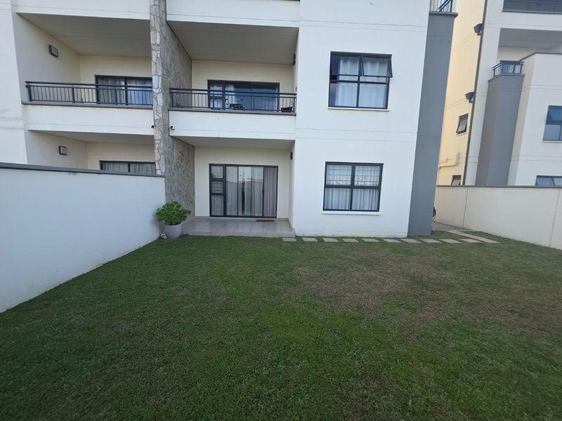 Rear view of the apartment building featuring a private garden, tiled patio area, and upper-level balconies with stone accents.