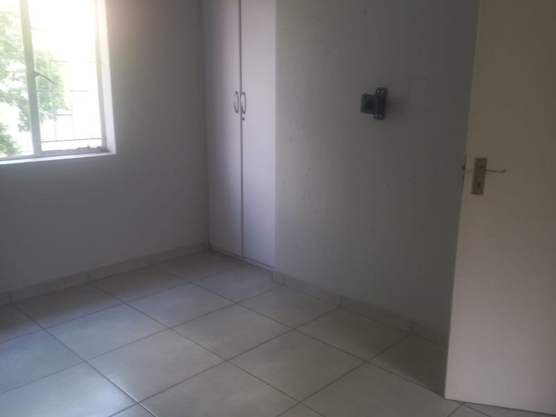 A bright, empty bedroom featuring neutral tiled flooring, a built-in wardrobe, and a window fitted with security bars.