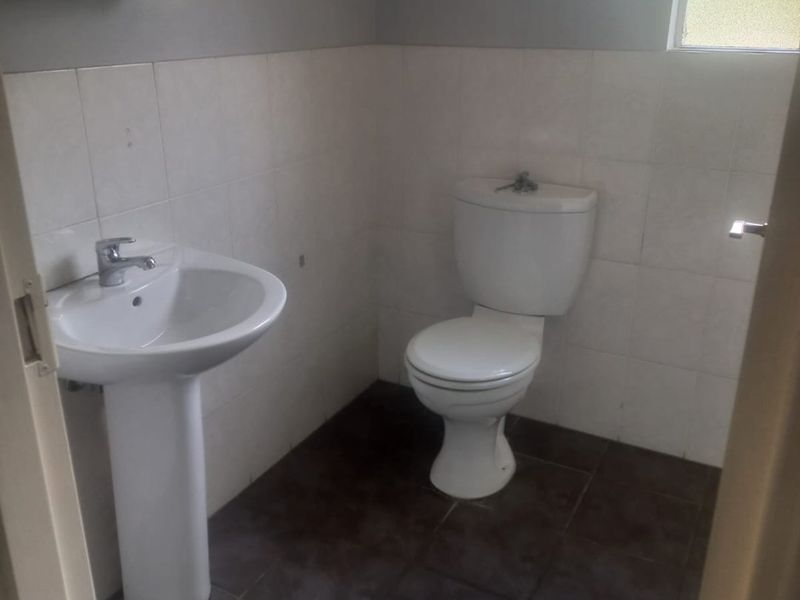 A functional guest bathroom featuring a pedestal basin, toilet, tiled flooring, and neutral wall finishes.