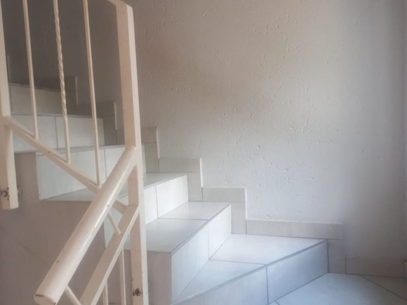 A functional staircase featuring white tiled steps and a simple metal balustrade, providing access between levels in the townhouse.