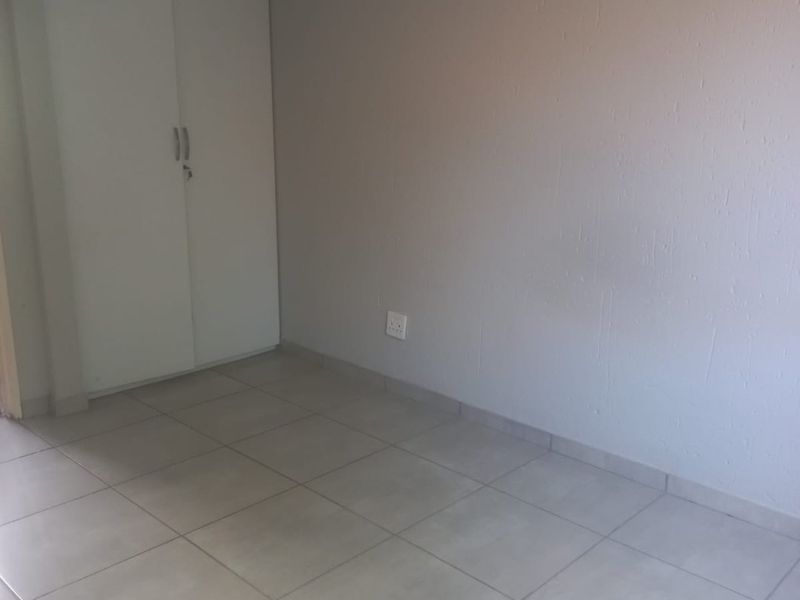 A clean, empty bedroom featuring neutral tiled flooring and a built-in white wardrobe, providing a blank canvas for personalization.