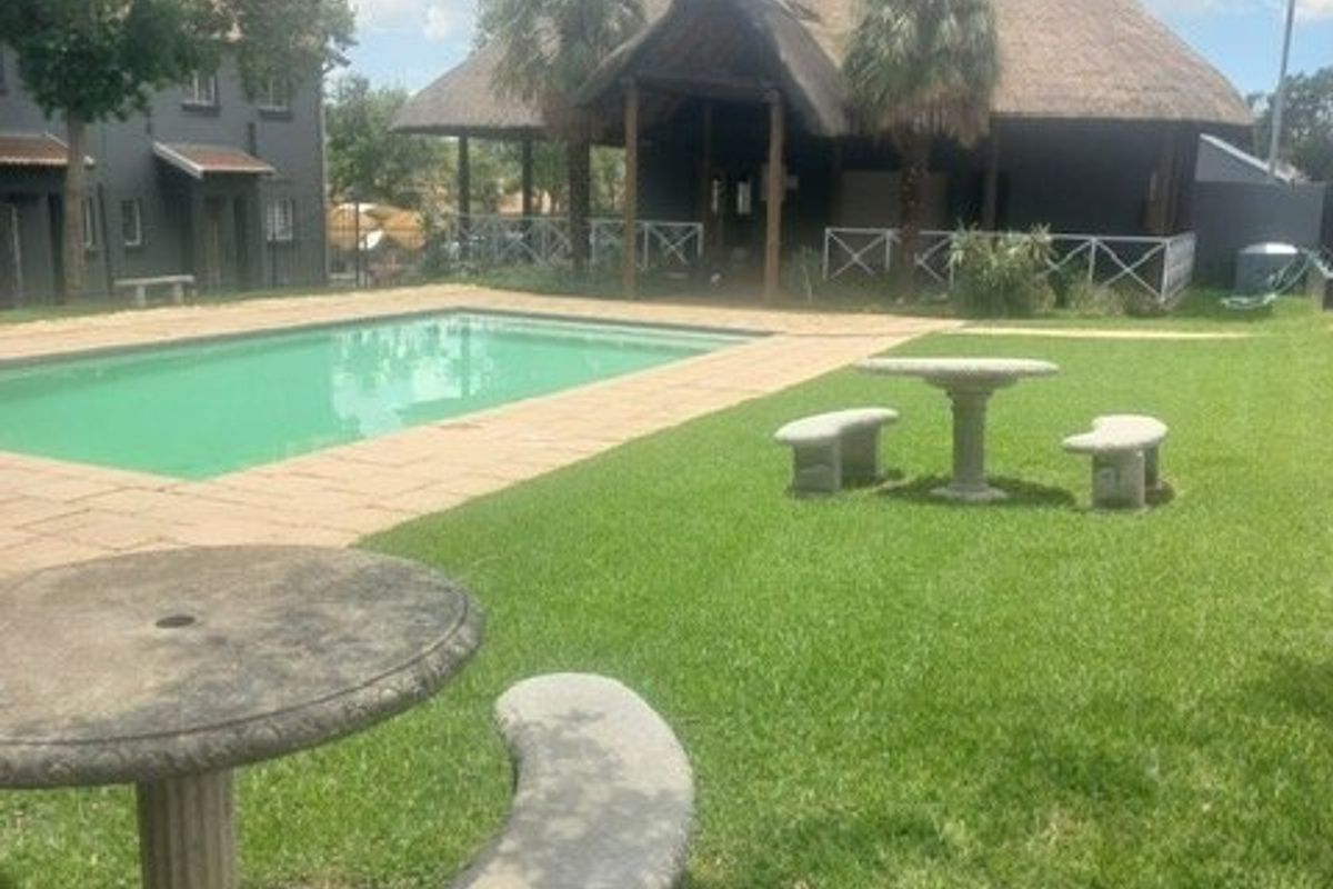 Outdoor pool area featuring a swimming pool, paved surround, and a large thatched lapa structure set within a landscaped garden.