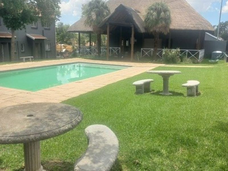 Outdoor pool area featuring a swimming pool, paved surround, and a large thatched lapa structure set within a landscaped garden.