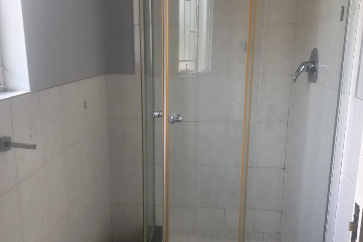 A functional bathroom featuring a curved glass shower enclosure with tiled walls and flooring, requiring minor cosmetic updates to improve its overall appeal.