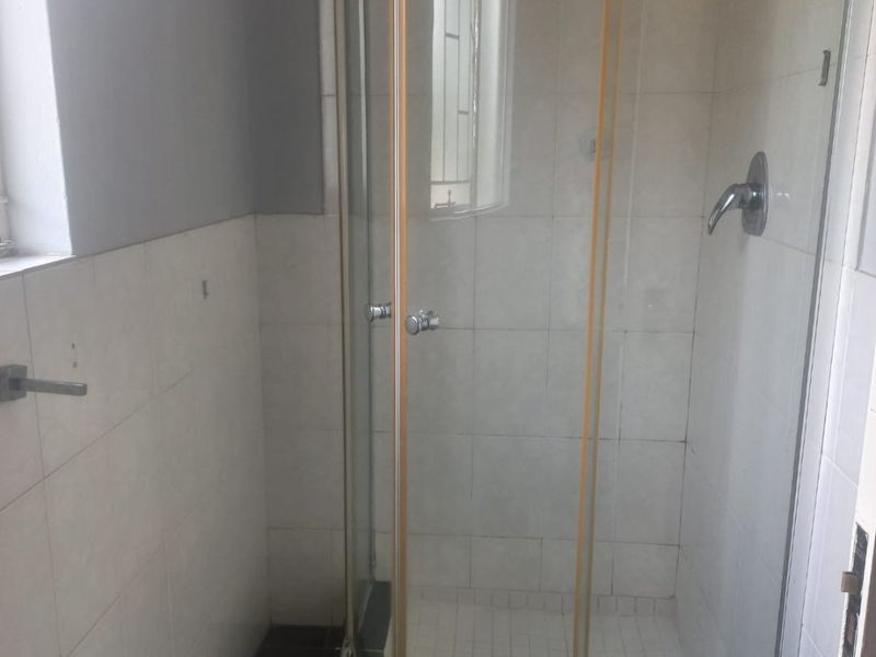 A functional bathroom featuring a curved glass shower enclosure with tiled walls and flooring, requiring minor cosmetic updates to improve its overall appeal.