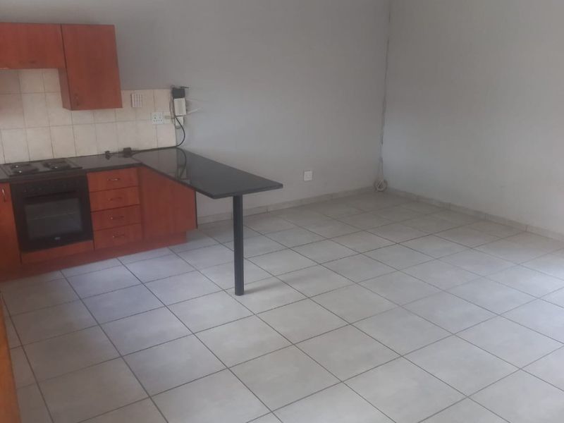 An empty open-plan kitchen and living area featuring tiled flooring, built-in cabinetry with an integrated oven, and a breakfast bar.