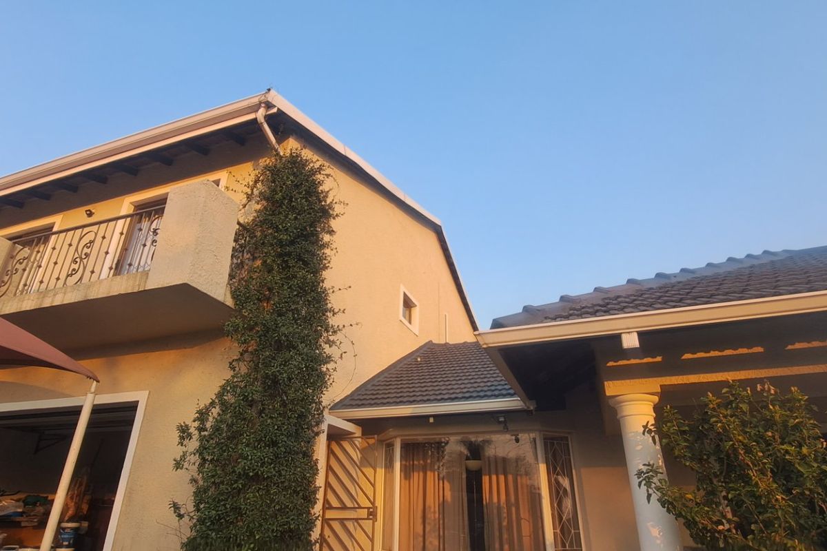 Rear exterior view of the apartment building featuring a balcony with wrought iron railing, tiled roofing, and established garden elements.