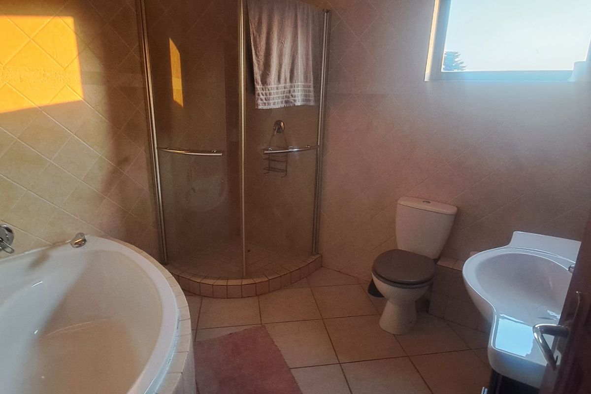 A functional bathroom featuring a corner bathtub, separate glass shower enclosure, pedestal washbasin, and toilet with neutral wall and floor tiling.