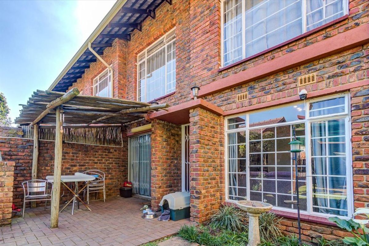 Rear exterior view of a brick townhouse featuring a paved patio area with a timber pergola and large windows.