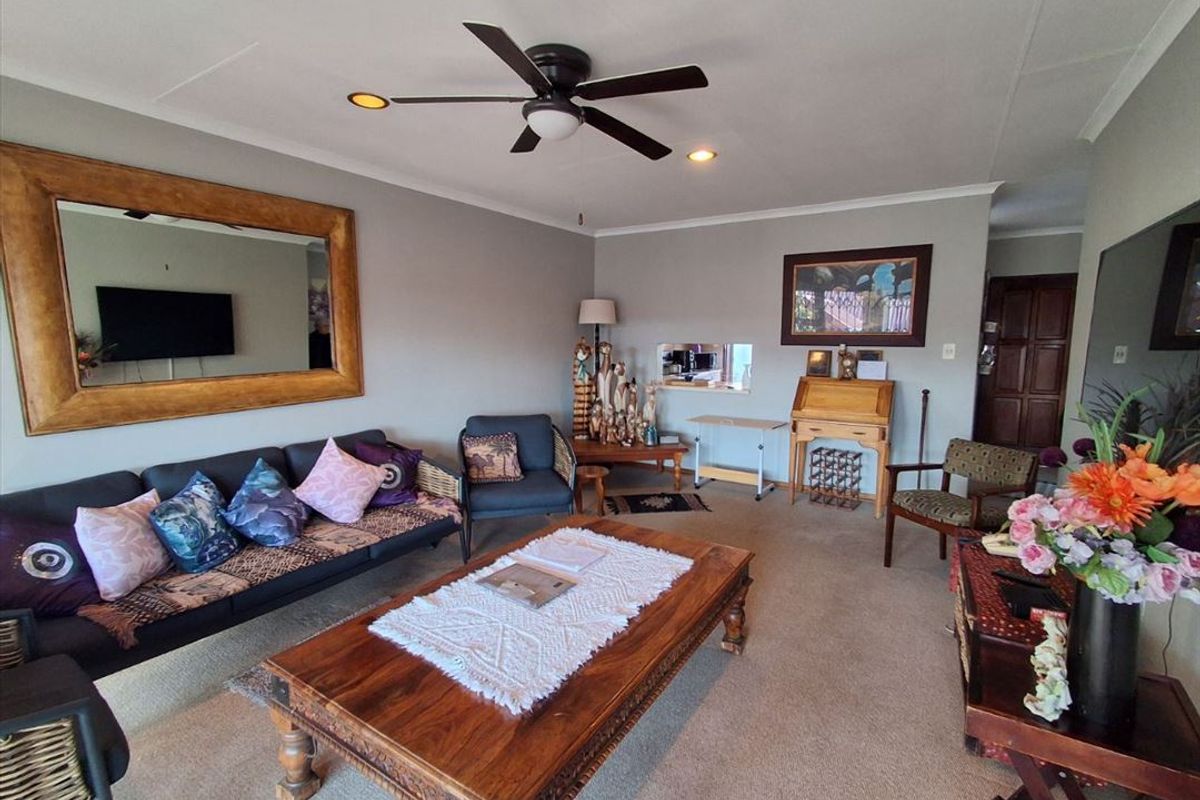 A comfortable living room featuring a ceiling fan, recessed lighting, and a convenient pass-through window connecting to the adjacent kitchen area.