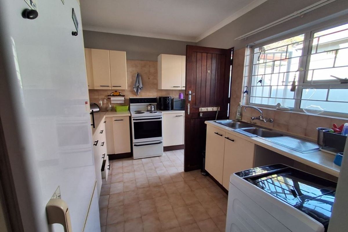 A functional kitchen featuring built-in cabinetry, a double basin sink, tiled flooring, and a freestanding stove with direct access to the exterior.
