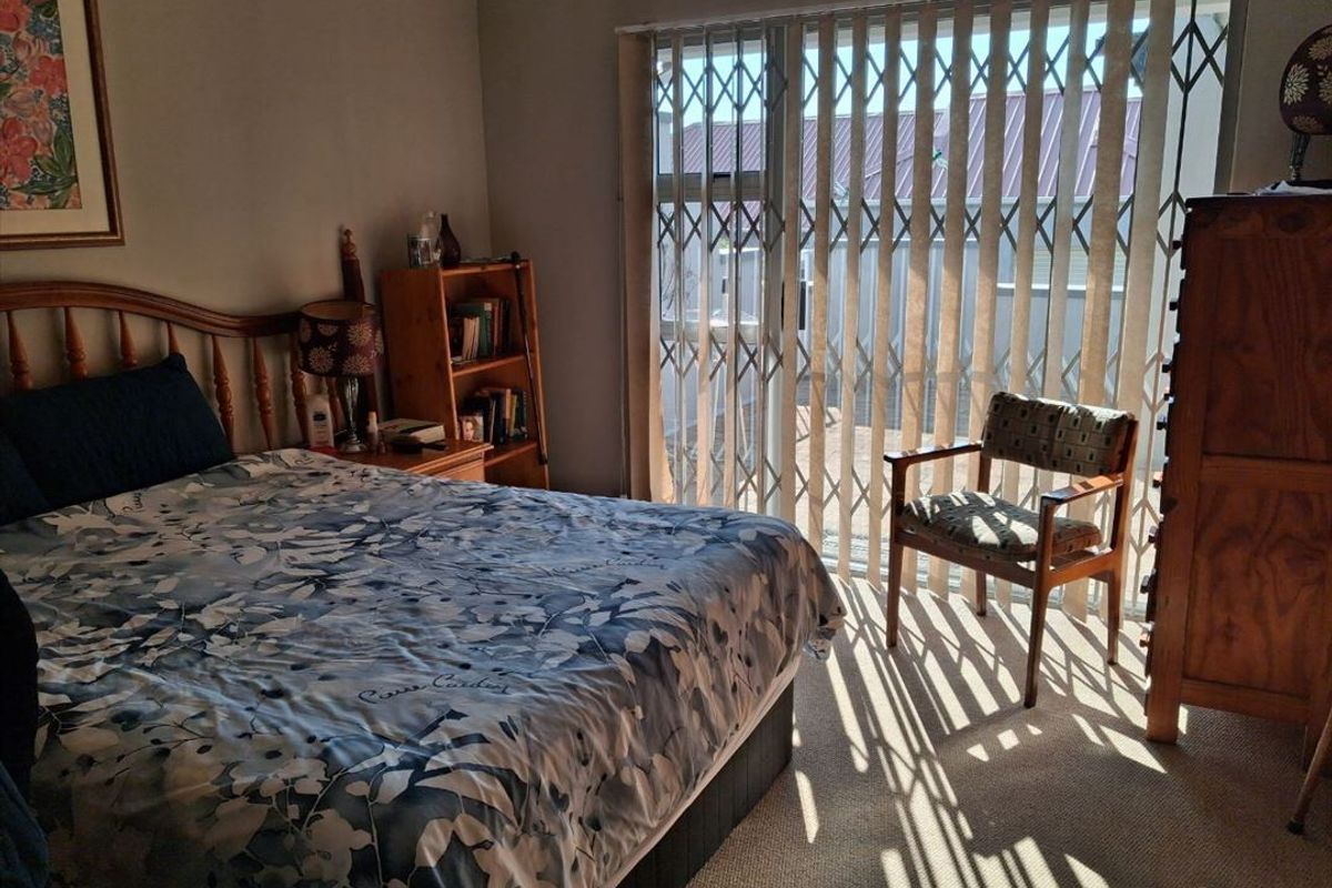 A bedroom featuring carpet flooring, vertical blinds, and a sliding glass door with an integrated security gate providing access to the exterior.